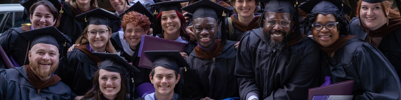 A large group of just-graduated students posing with their diploma covers