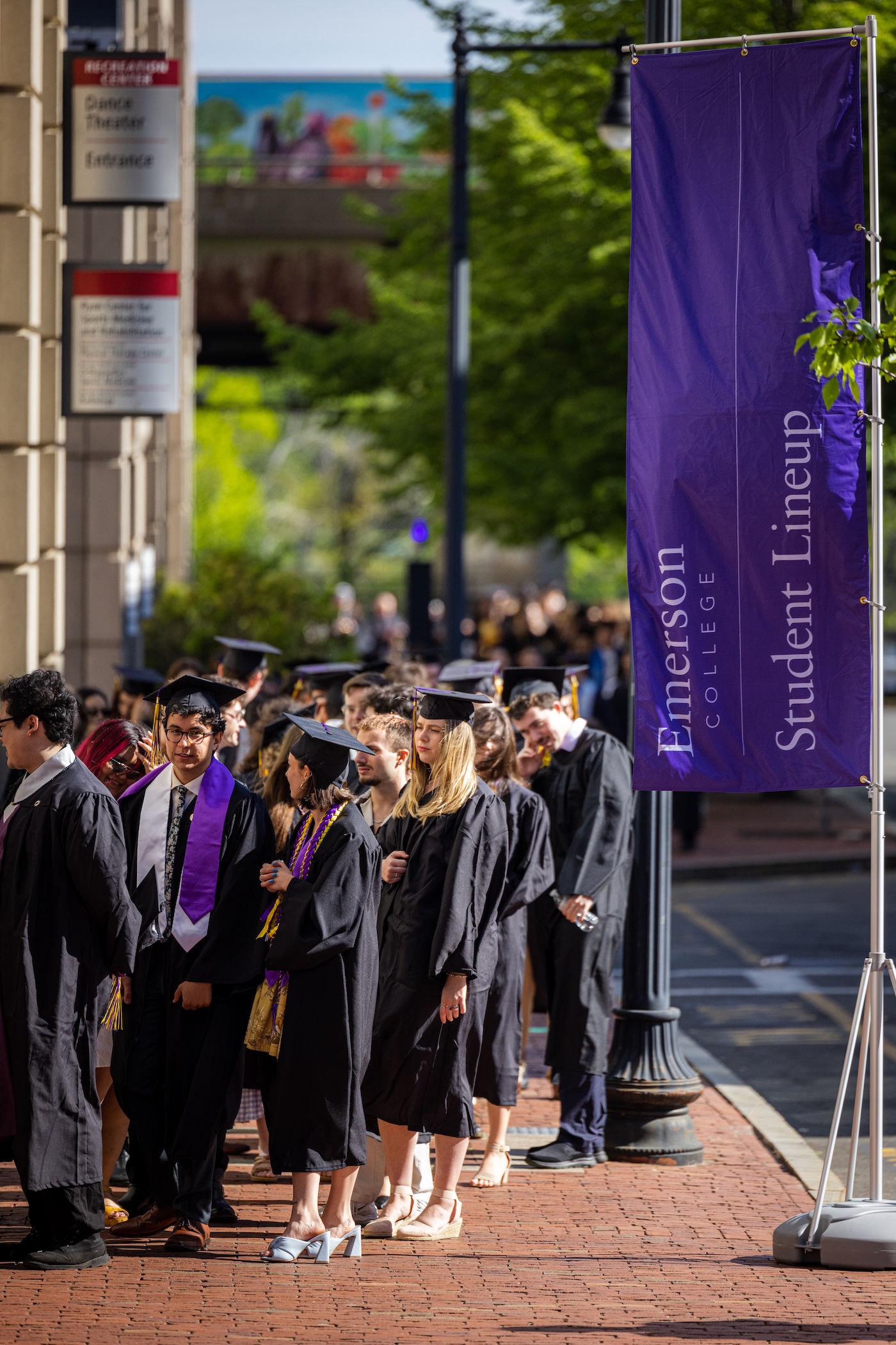Students in the sidewalk queuing for their ceremony next to a flag that says Student Lineup